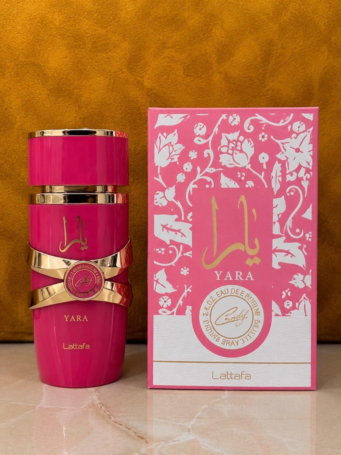 Frasco rosa de Lattafa Yara junto a su caja sobre fondo dorado